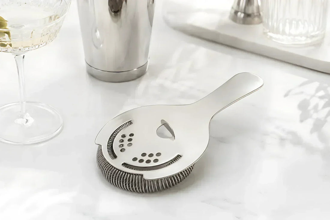 A Hawthorne strainer placed beside a Boston shaker tin