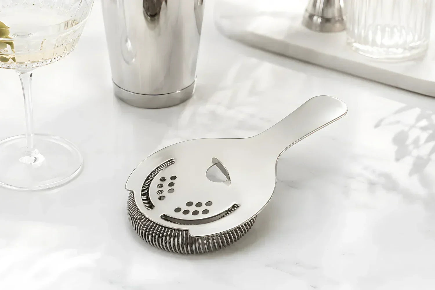 A Hawthorne strainer placed beside a Boston shaker tin