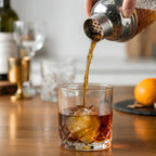 glass cocktail shaker pouring a cocktail into a glass