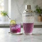 glass cocktail shaker placed next to a cocktail