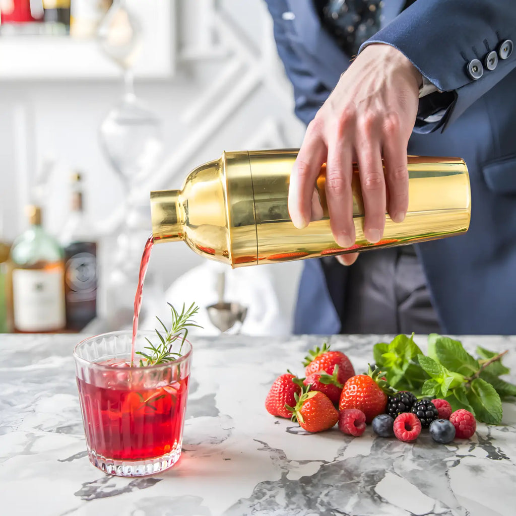 gold cobbler shaker pouring a cocktail into a glass