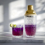 gold glass cocktail shaker placed next to a cocktail