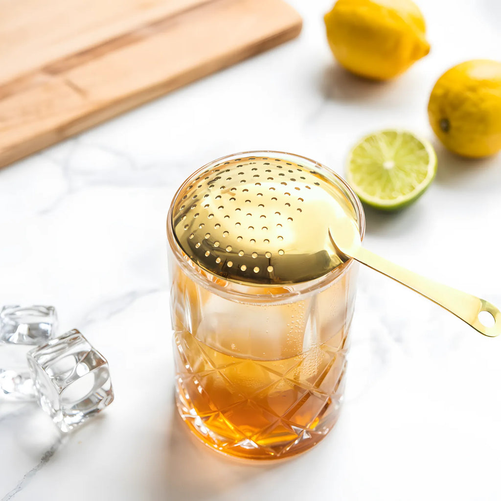 gold Julep strainer resting on a mixing glass