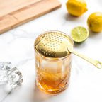 gold Julep strainer resting on a mixing glass