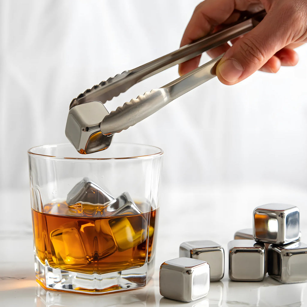ice tongs placing a stainless steel ice cube into a glass of whiskey